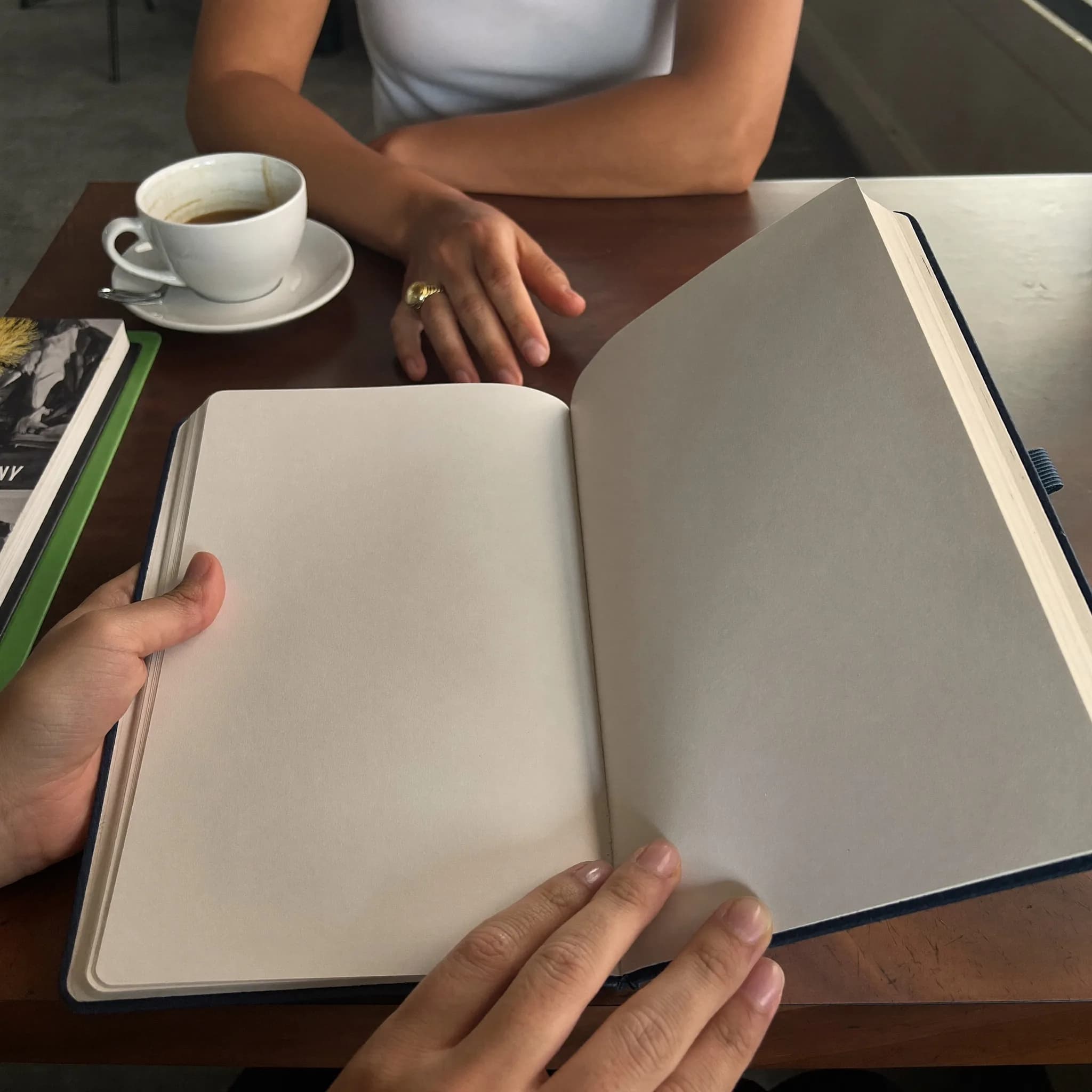 Two women's hands resting over a notebook and a cup of tea