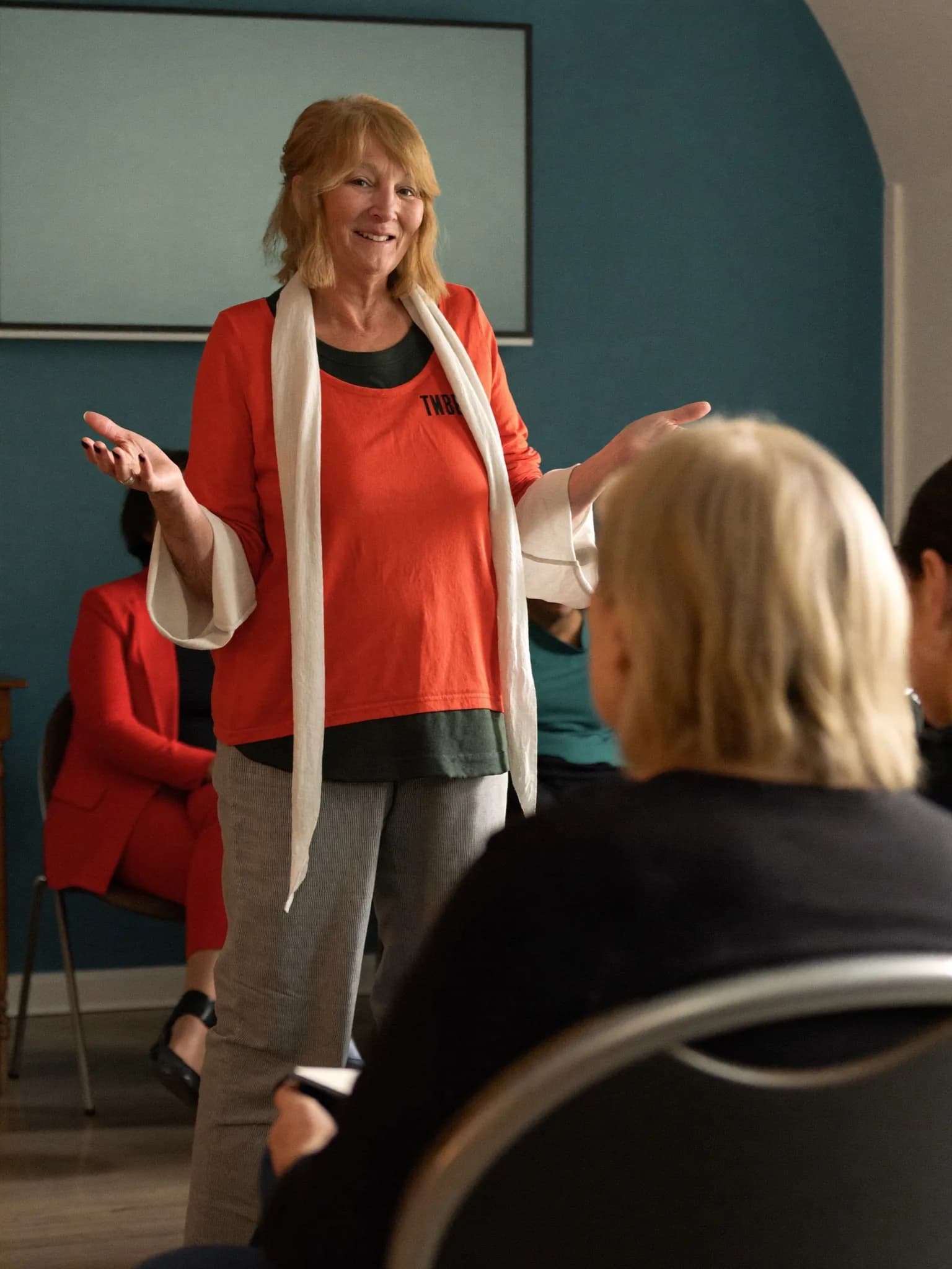 A woman speaking warmly to a small group in a community room