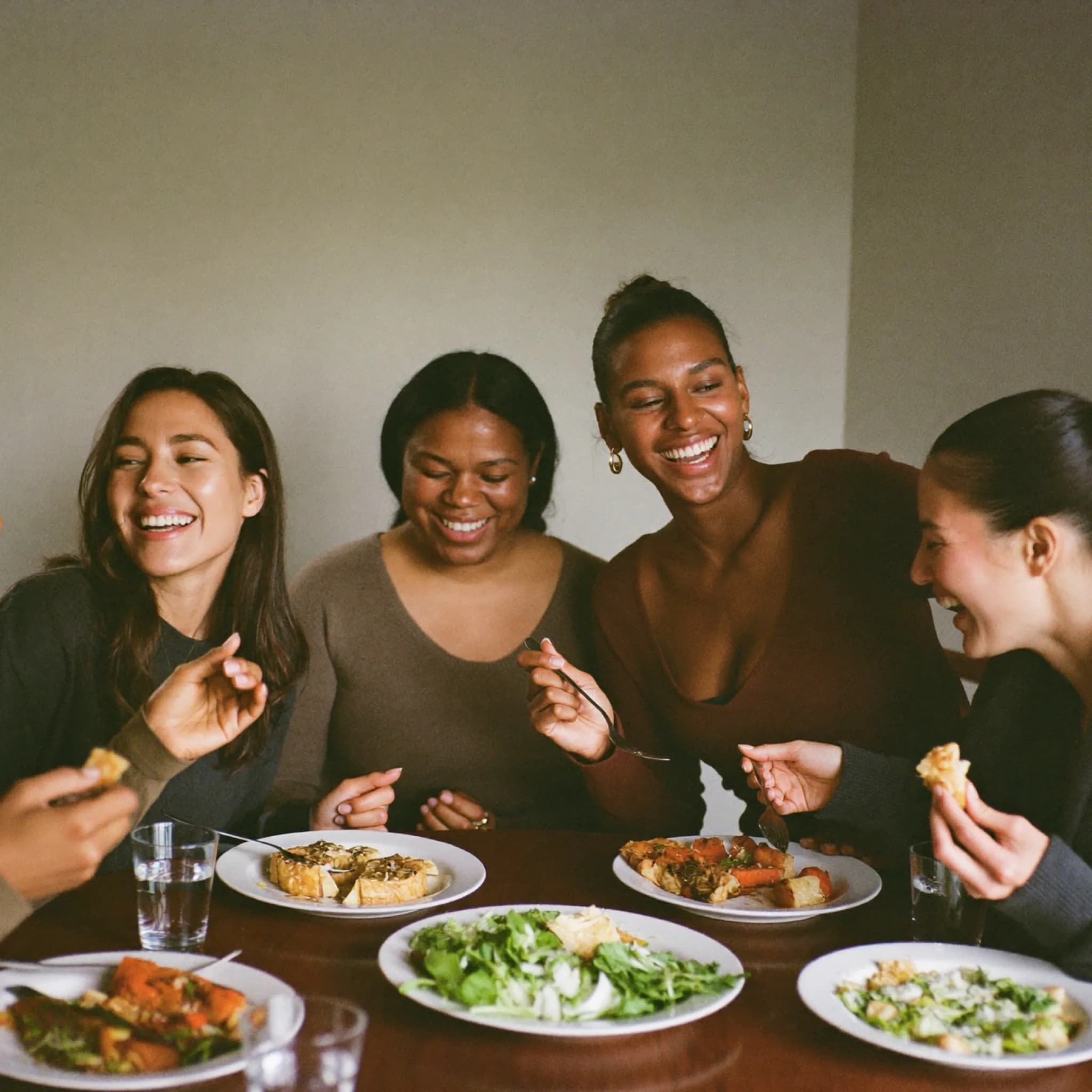 Four women laughing together over a shared meal at a kitchen table